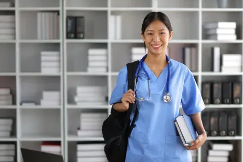 Nursing student smiling in library with bag over shoulder